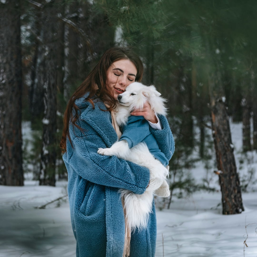 a woman holding a white dog in the snow.